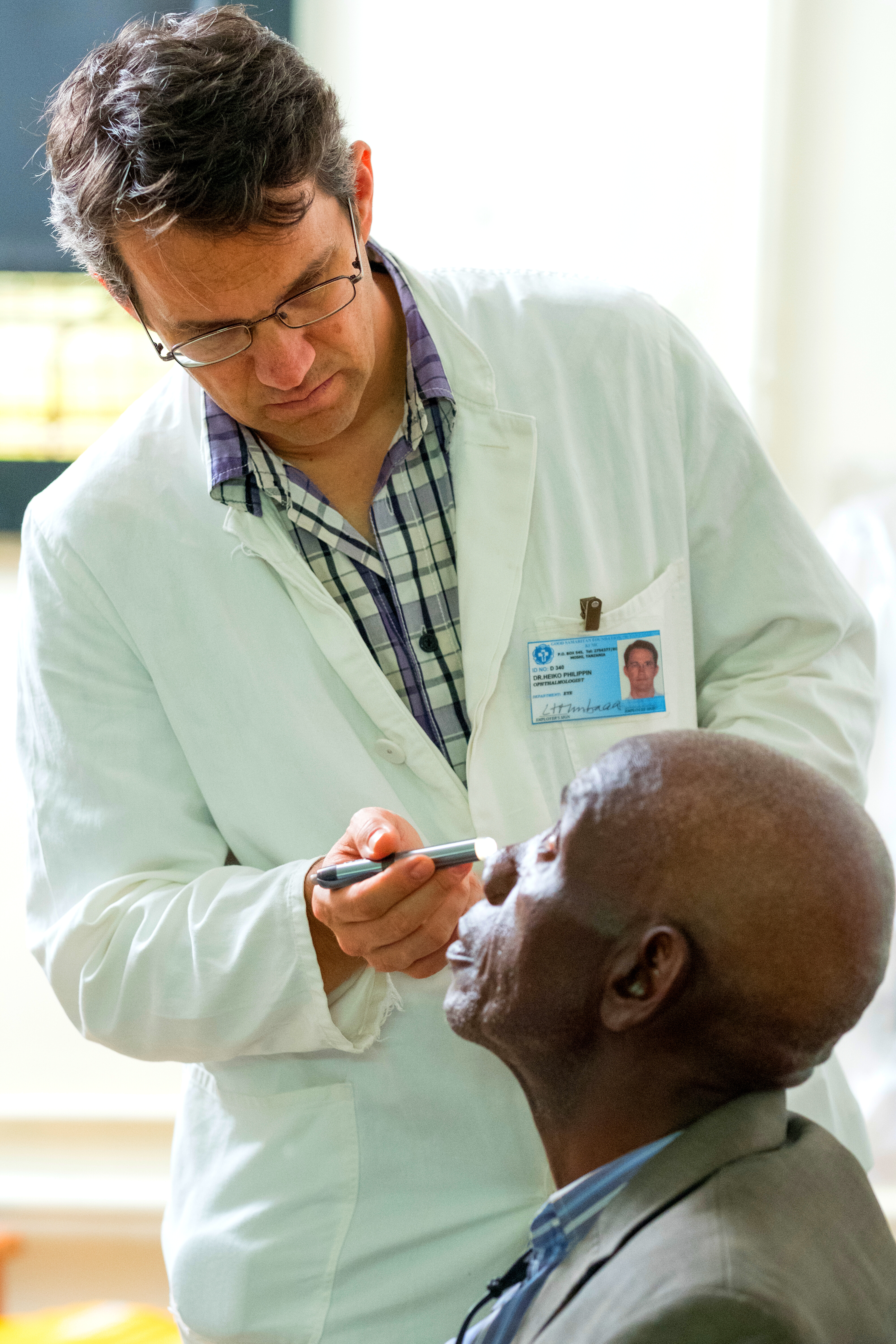 a doctor stands while using a pen torch to inspect a patient's eyes
