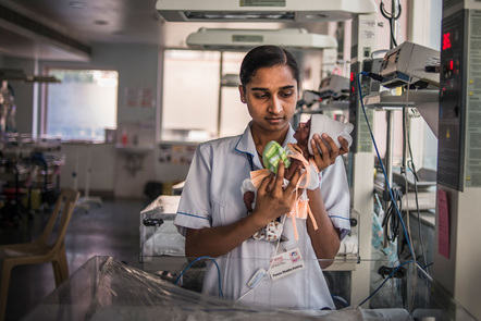 Image of nurse holding premature baby in front of medical equipment