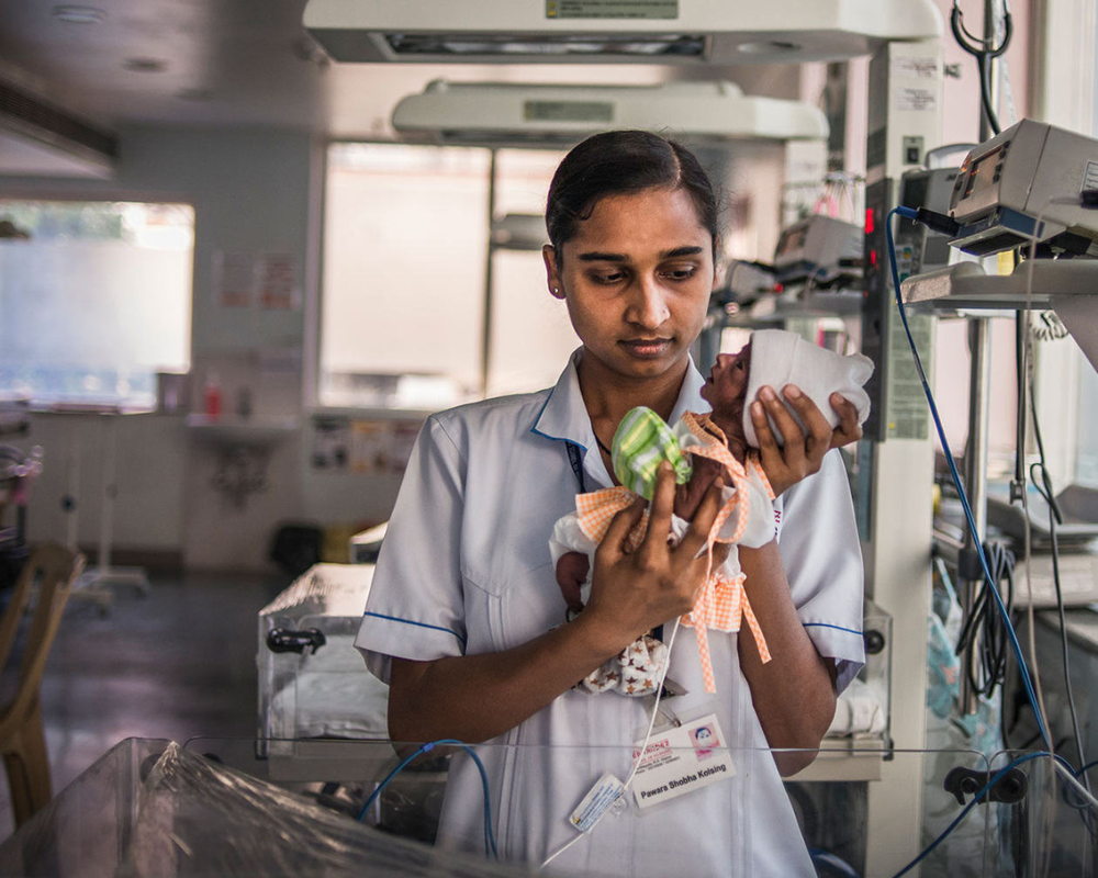 Image of nurse holding premature baby in front of medical equipment