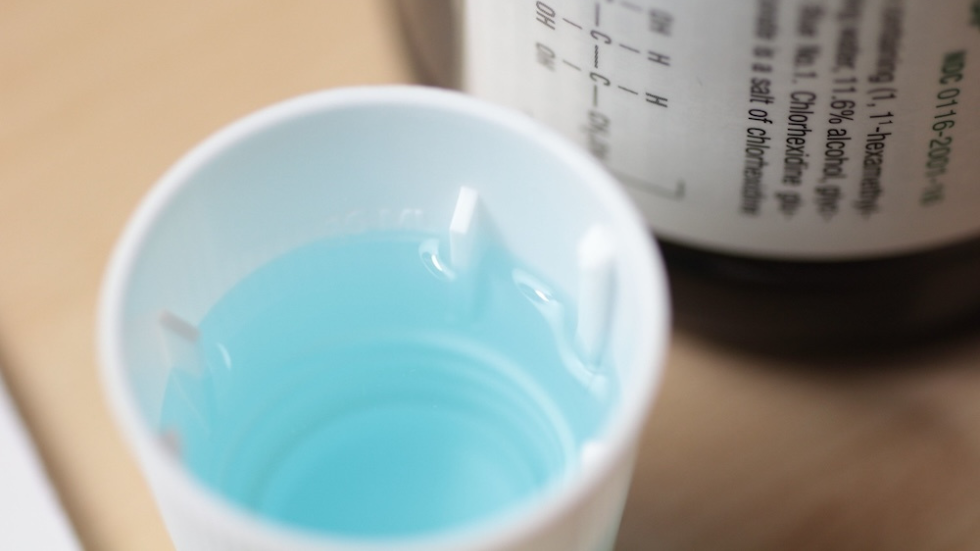 a blue liquid in a plastic cup next to a bottle with chemical symbols