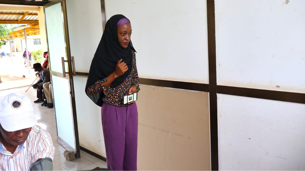 a woman in a hijab holds up a phone with an 'E' symbol for acuity testing