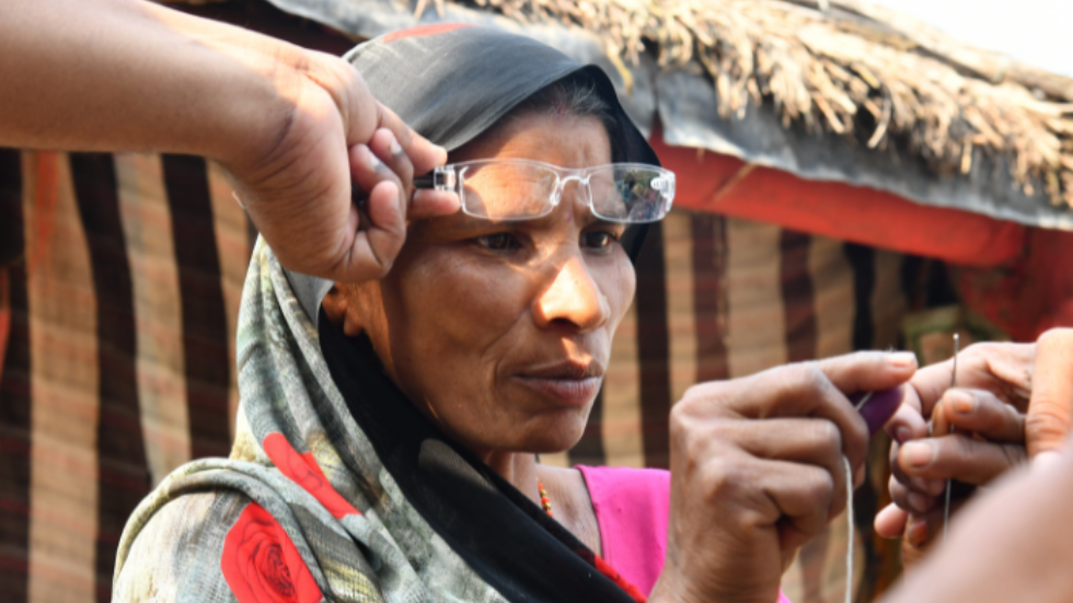 In India, a woman tries on glasses while sewing