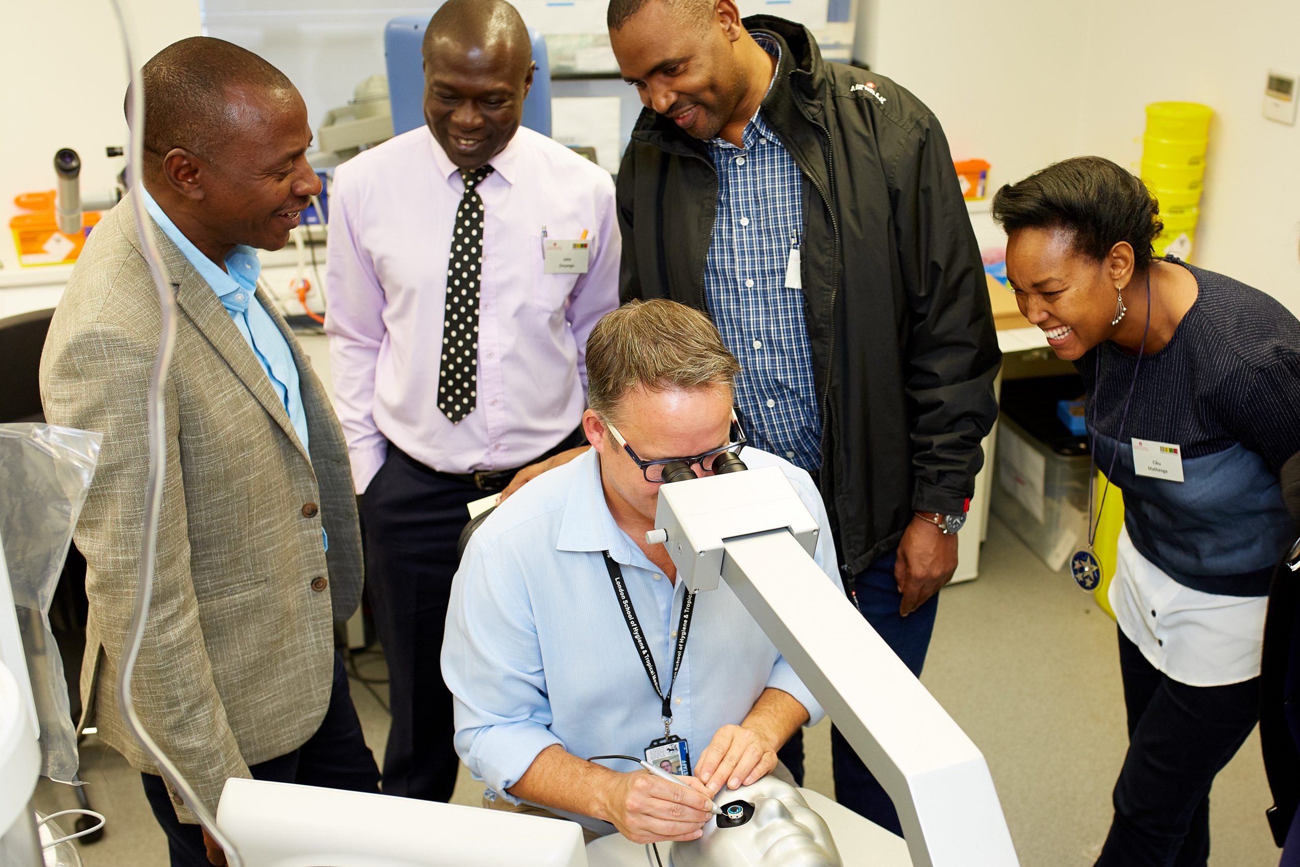 a man uses a microscope for surgical skills while four people observe 