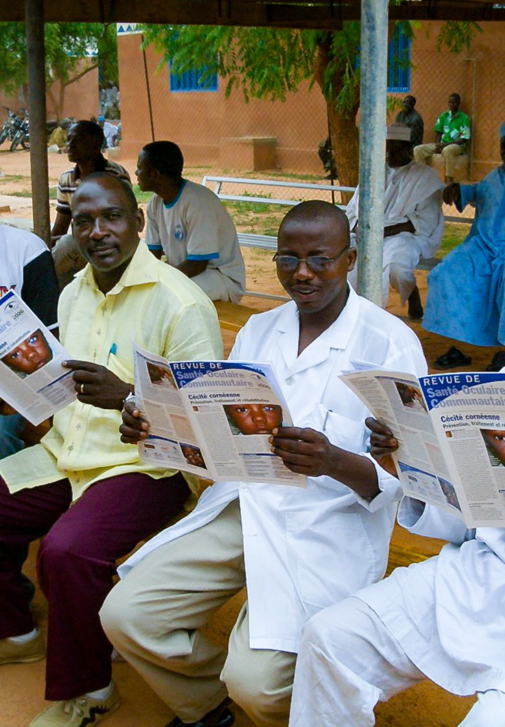 a group of men sit on a bench and read the journal
