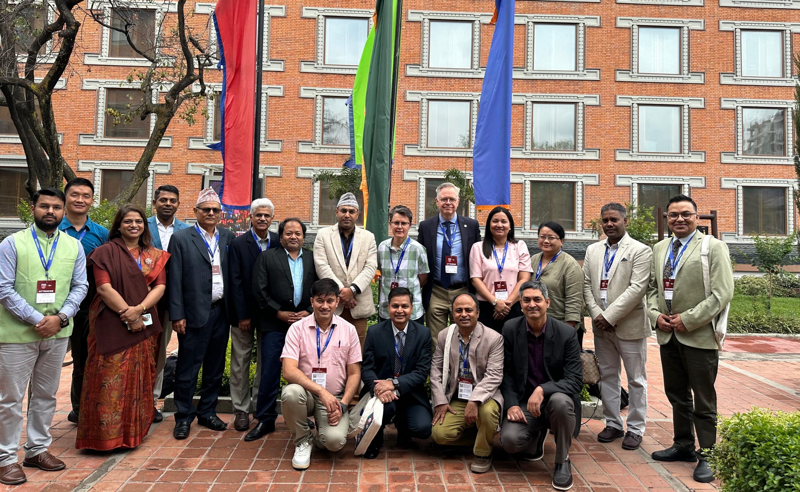 a group of ICEH and NNJS colleagues stand and pose for a photo in front of some flags