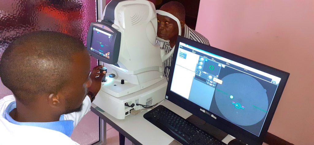 a photo of a man behind screens and equipment, with a patient sitting at the equipment