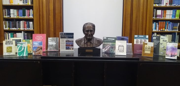 A photograph of the Library book display, showing thirteen brightly coloured books on a cabinet surrounding a metal bust of Sir Richard Doll.