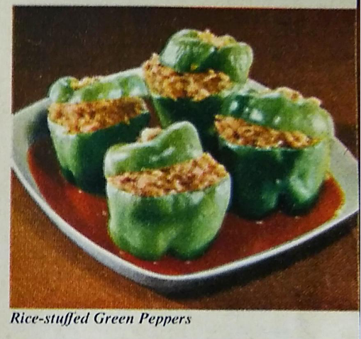 A colour photograph from American Rice: My Home Cook Book depicting rice-stuffed green peppers. The rice is brownish in colour and the peppers are sitting in a gravy on the plate.