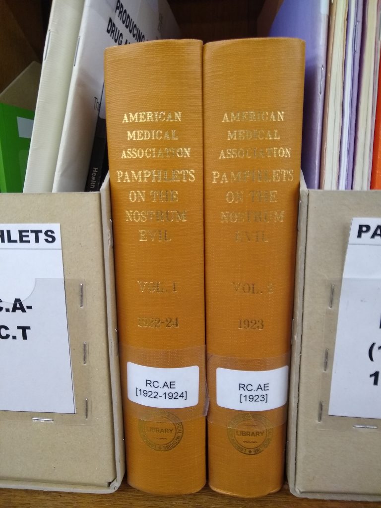 Photograph of the spines of the two volumes of "American Medical Association: Pamphlets on the Nostrum Evil" in place on the shelves.