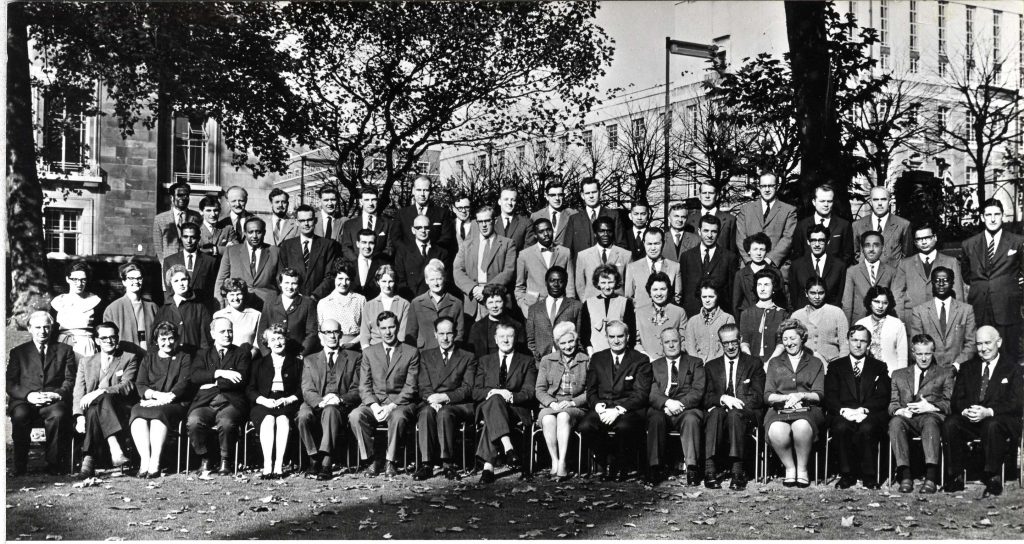 Black and white photograph of LSHTM staff outside the Keppel Street building. Shows four rows of men and women and Margot Davies in a skirt and blazer on the front row.