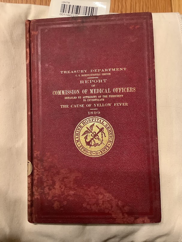 Cover of 'Report of Commission of Medical Officers detailed by authority of the president to investigate The Cause of Yellow Fever 1899' in red with the title of the book and the navy insignia embossed in gold.