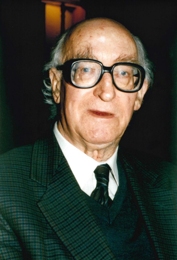 Photograph of William Brass wearing glasses and a suit