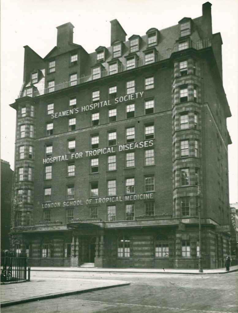 Large, several story brick building with sign reading 'Seamen's Hospital Society Hospital for Tropical Diseases, London School of Tropical Medicine. 