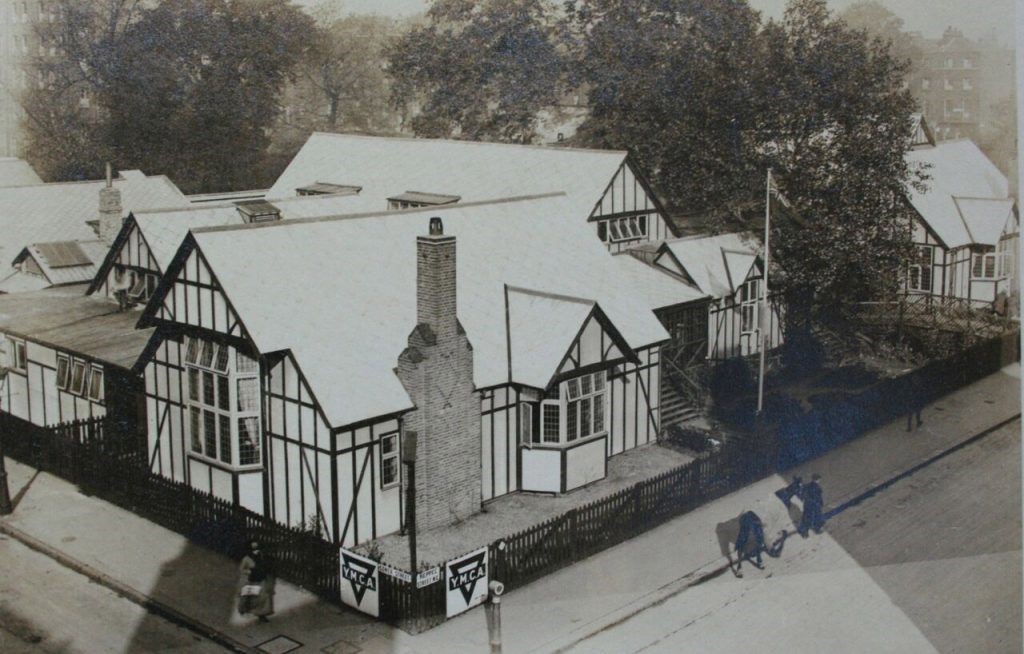 Single story building with a white roof and walls, and black paneling surrounded by a short fence. A logo for YMCA is visible in the front of the image. 