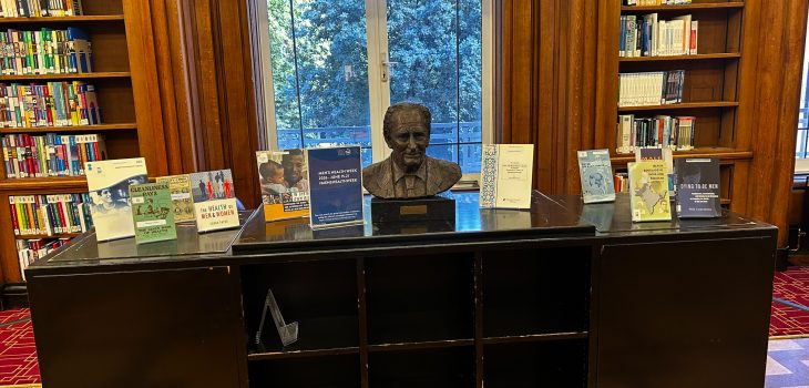 A desk in the library. With a bust in the middle surronded by books about